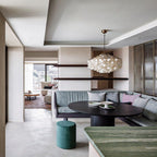 Gold-ringed Clérachic shell chandelier over an oval black table and a green banquette in an open-plan room.