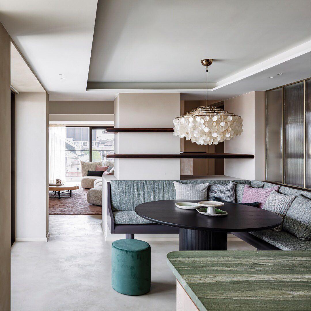 Gold-ringed Clérachic shell chandelier over an oval black table and a green banquette in an open-plan room.