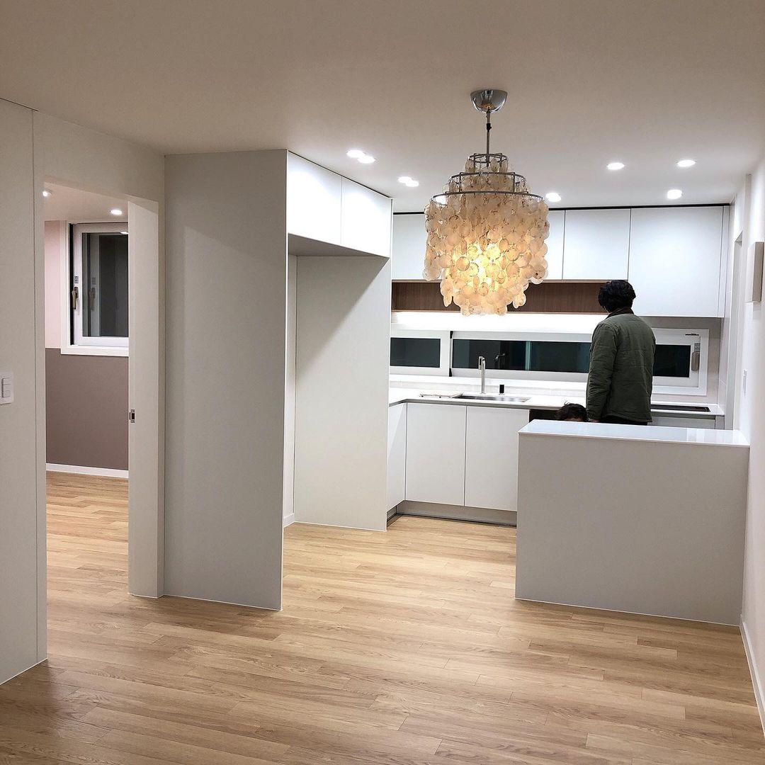 Clérachic shell chandelier lit in a white kitchen with an oak floor and a person standing at the counter.