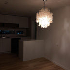 Lit Clérachic shell chandelier glowing in a dim, unfurnished kitchen, its discs bright against the dark room.