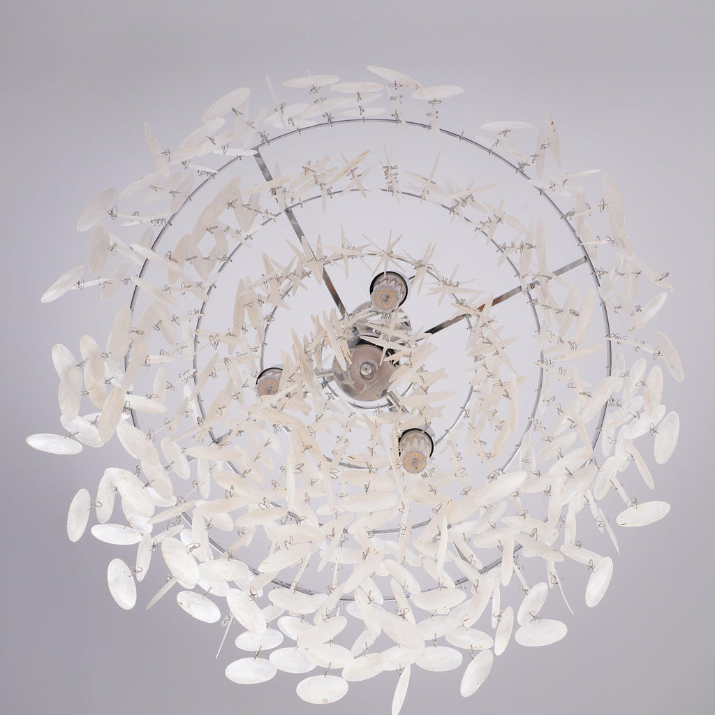 Looking straight up into a chrome-ringed Clérachic shell chandelier, three bulbs visible inside the spiral of white discs.