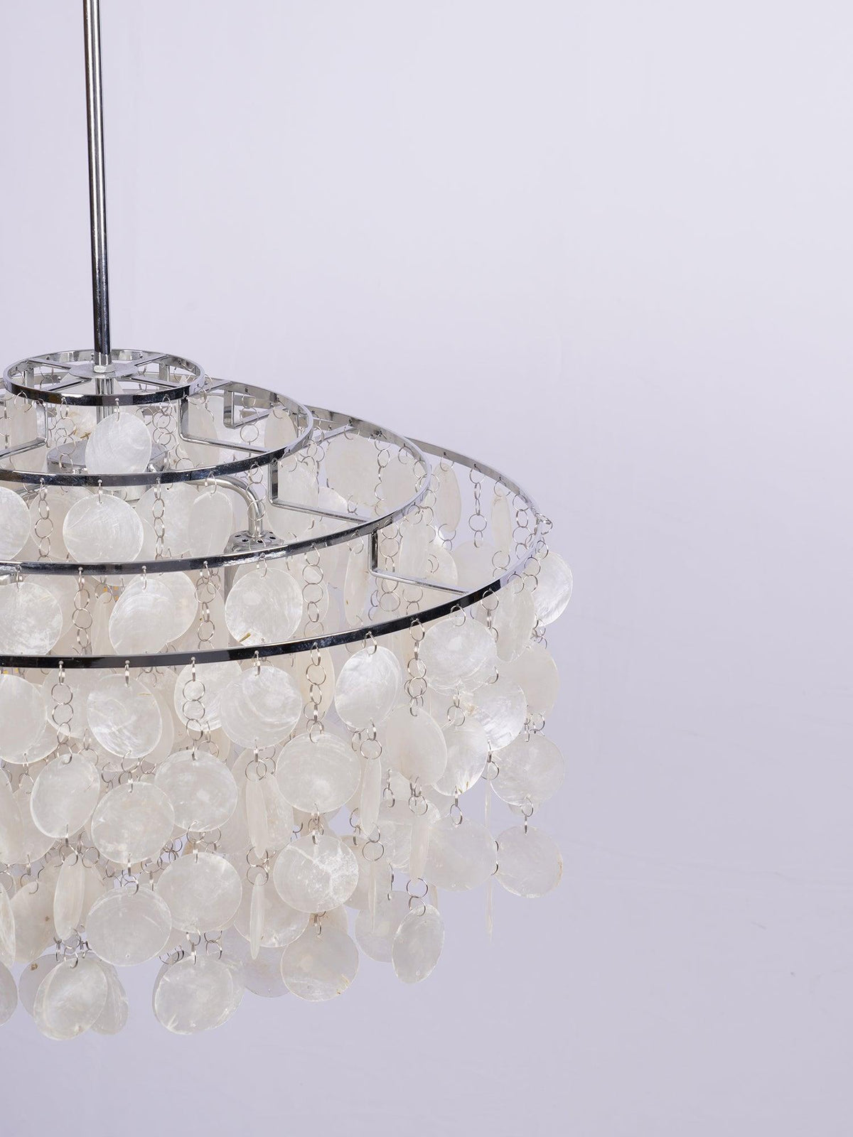 Close view of the stacked chrome rings and white discs on this Clérachic shell chandelier, against a pale lilac backdrop.
