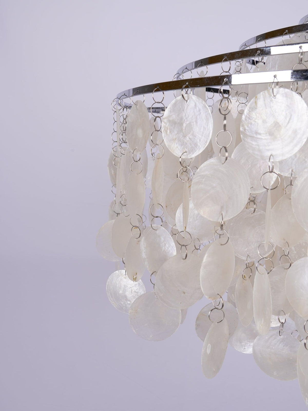 Close view of large pearly shell discs hanging on small metal rings from chrome hoops on this Clérachic chandelier.