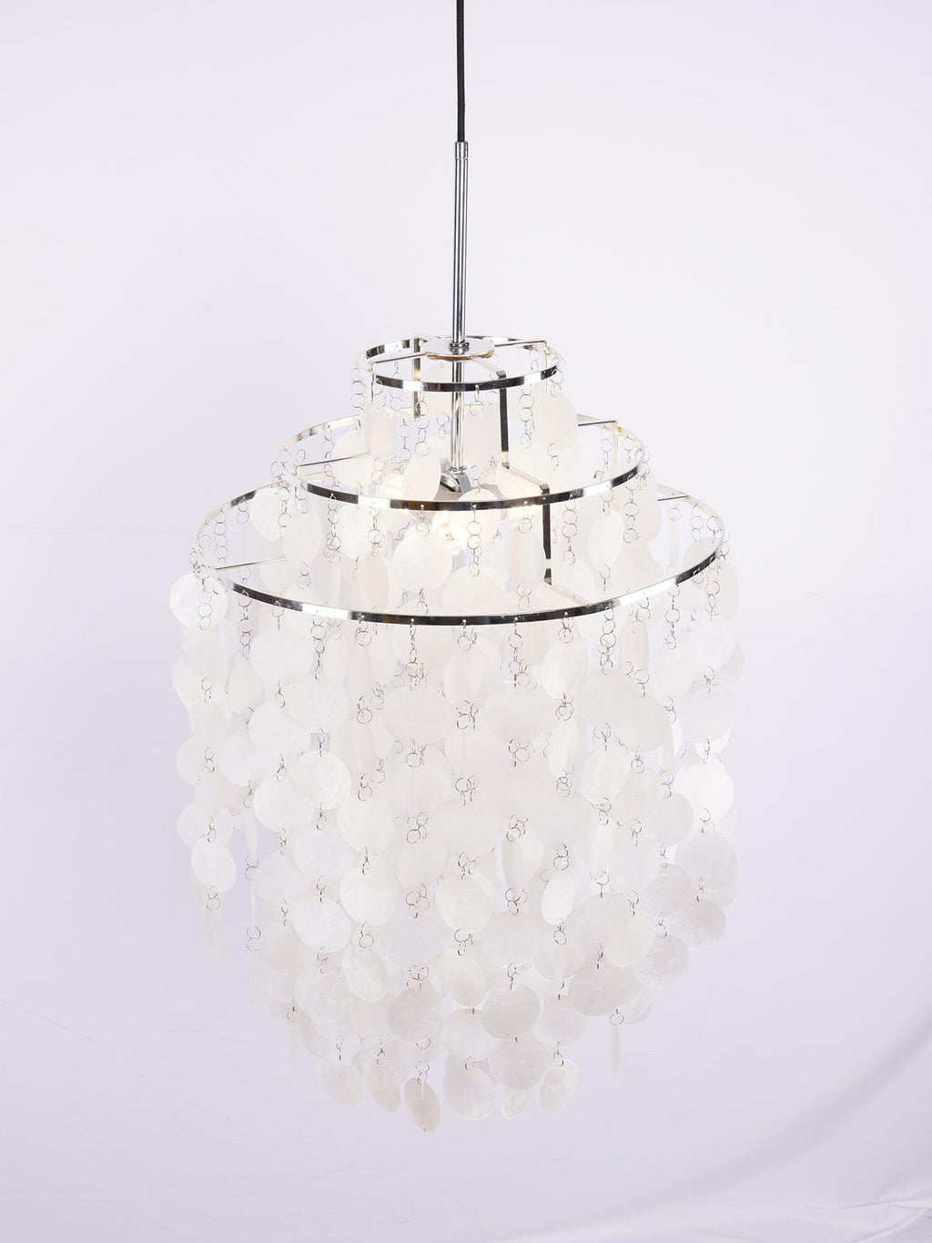 Narrow three-tier Clérachic shell chandelier with chrome rings, hung from a black cable against a pale lilac backdrop.