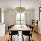 Clérachic shell chandelier centred over a long pale wood table and black chairs, in a room with a tall balcony window.
