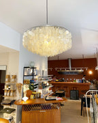 Lit Clérachic shell chandelier hung in a shop-café with a rust-red wall, a wicker counter and shelves of goods.