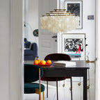Clérachic shell chandelier in a hallway above a dark table with a bowl of oranges, a velvet chair and framed prints.