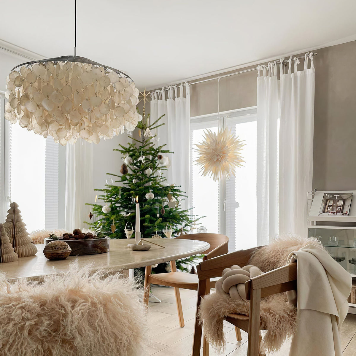 Clérachic shell chandelier at the corner of the frame in a bright dining room with a Christmas tree and sheepskin throws.