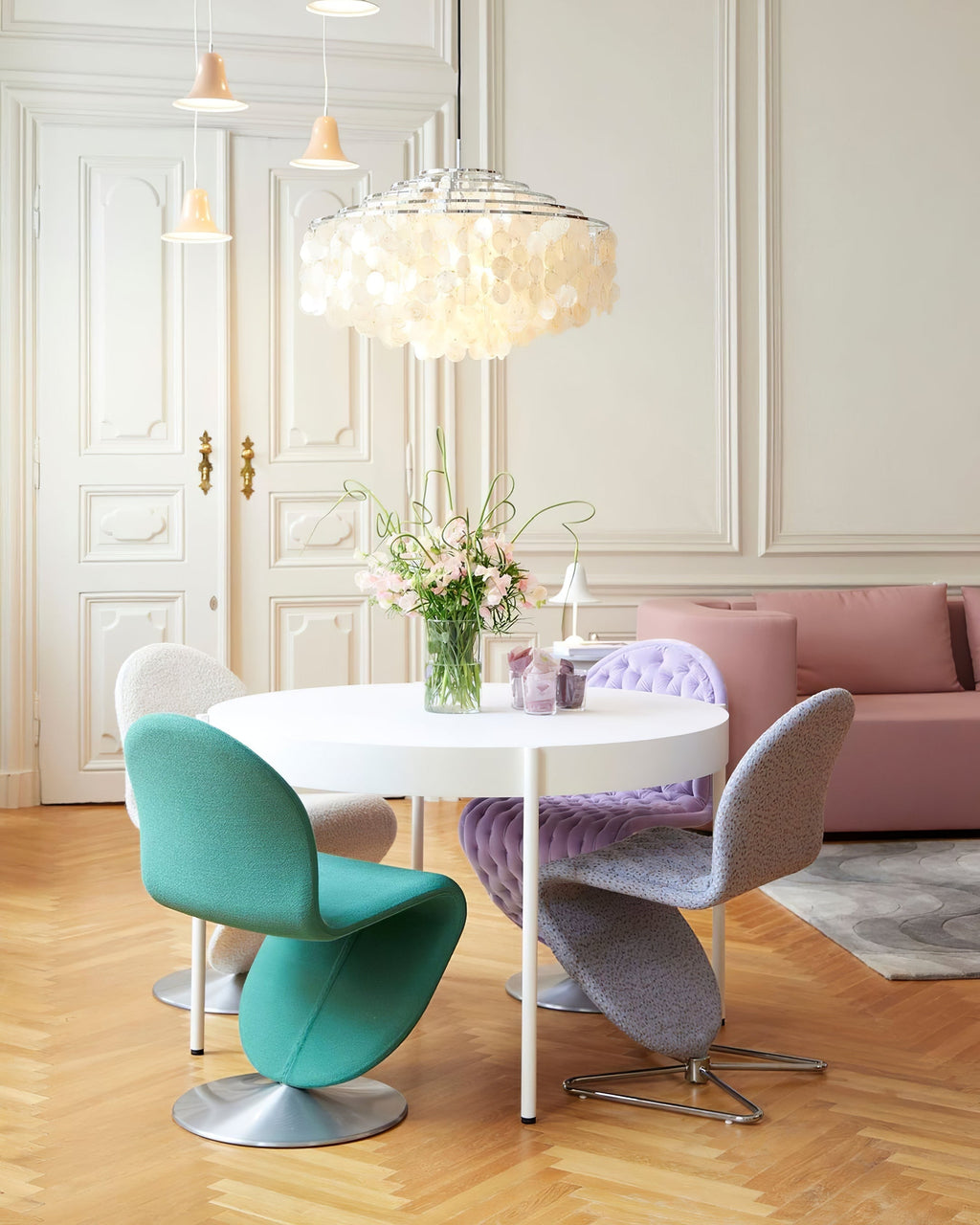 Clérachic shell chandelier over a round white table with turquoise and lilac chairs, in a room with panelled double doors.