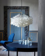 Chrome-ringed Clérachic shell chandelier against a blue-grey wall with a navy table, glassware and a blue chair below.