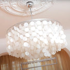 Looking up at a Clérachic shell chandelier with a chrome cap, below an ornate white ceiling rose and a warm pink wall.