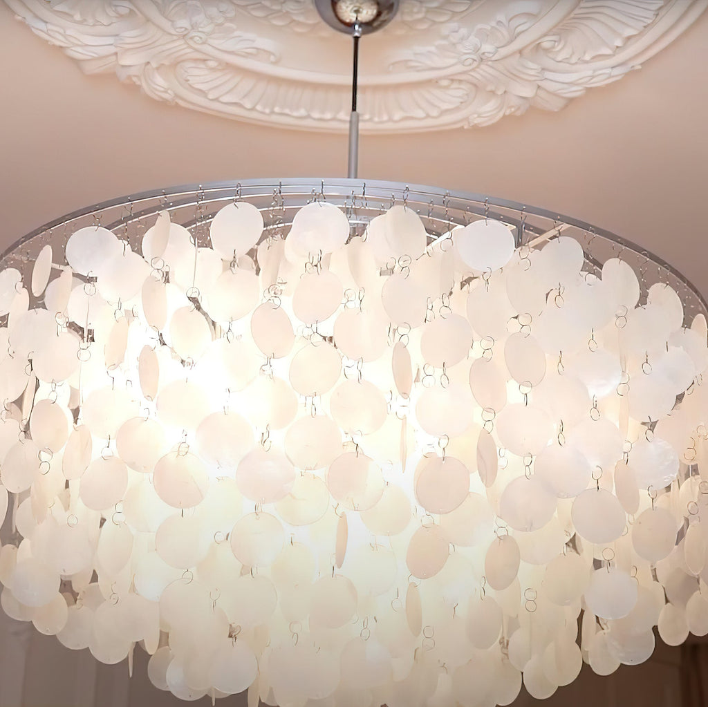Close view of the lit shell discs inside a wide Clérachic chandelier, below a chrome cap and a plasterwork ceiling.