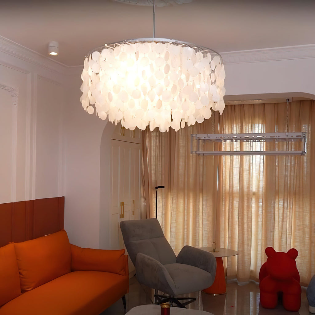 Large lit Clérachic shell chandelier with a silver rim in a living room with an orange sofa and a grey armchair.