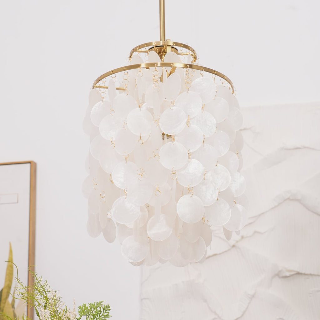 Close view of a gold-ringed Clérachic shell chandelier, white discs on small links, against a white textured wall.