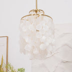 Close view of a gold-ringed Clérachic shell chandelier, white discs on small links, against a white textured wall.