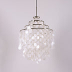 Three-tier chrome-ringed Clérachic shell chandelier, unlit, on a pale lilac backdrop with a black cable.