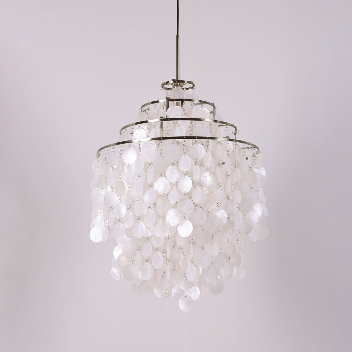 Three-tier chrome-ringed Clérachic shell chandelier, unlit, on a pale lilac backdrop with a black cable.