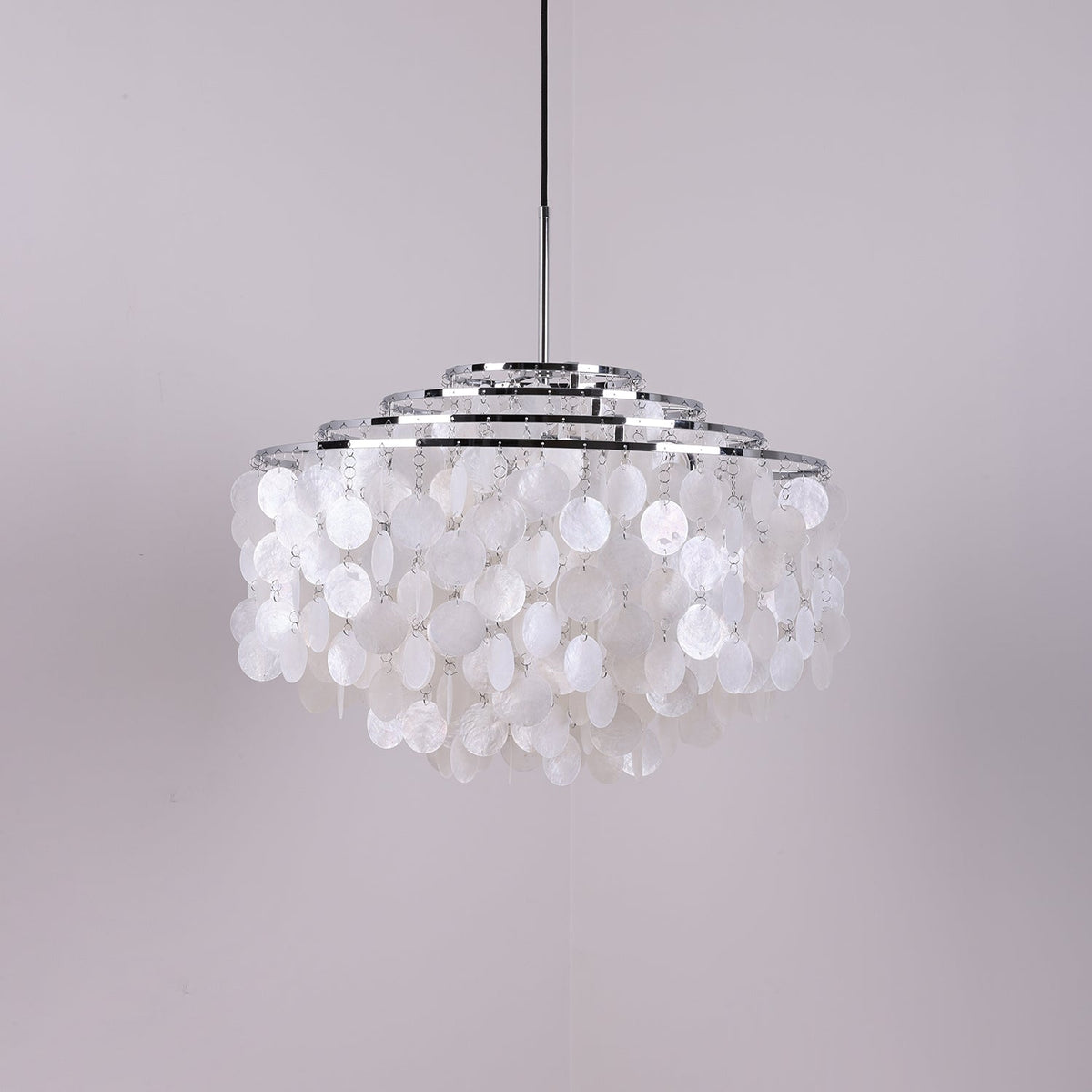 Wide chrome-ringed Clérachic shell chandelier, unlit, with white discs on a soft grey-lilac backdrop.