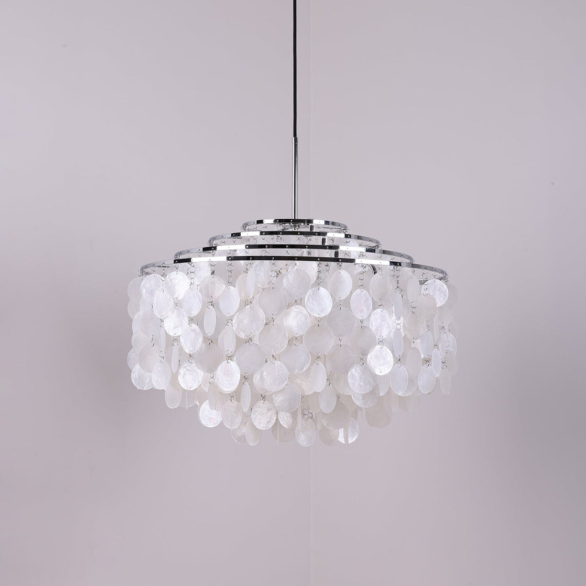 Chrome-ringed Clérachic shell chandelier on a grey-lilac backdrop, discs hanging in rounded layers below the rings.