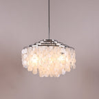 Lit Clérachic shell chandelier with chrome rings on a grey-pink backdrop, the discs glowing warm white from inside.