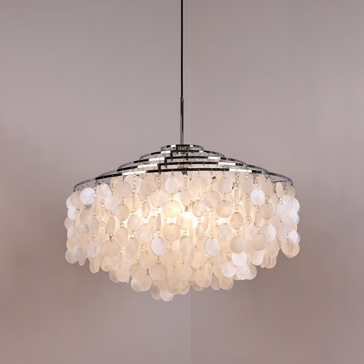 Lit Clérachic shell chandelier with a wide chrome crown, discs glowing warm and the bulbs faintly visible within.
