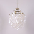 Unlit tall gold-ringed Clérachic shell chandelier with four tiers of white discs on a lilac-grey backdrop.