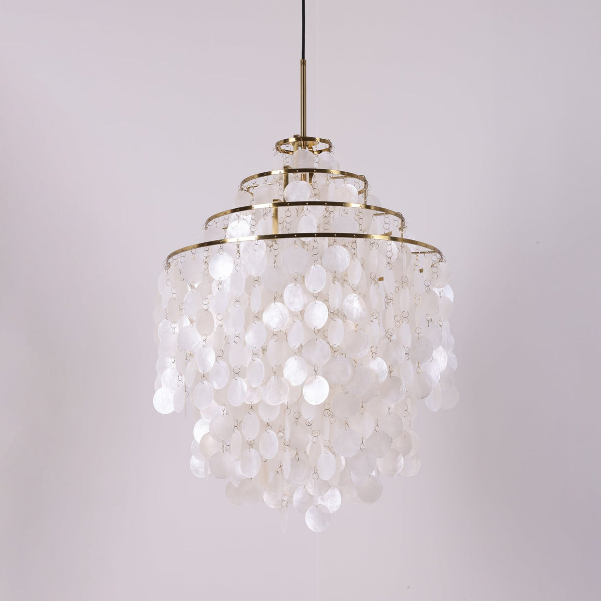 Unlit tall gold-ringed Clérachic shell chandelier with four tiers of white discs on a lilac-grey backdrop.