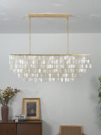 Unlit rectangular Clérachic shell chandelier with a gold bar and chains, its flat discs in rows, above a wooden sideboard.