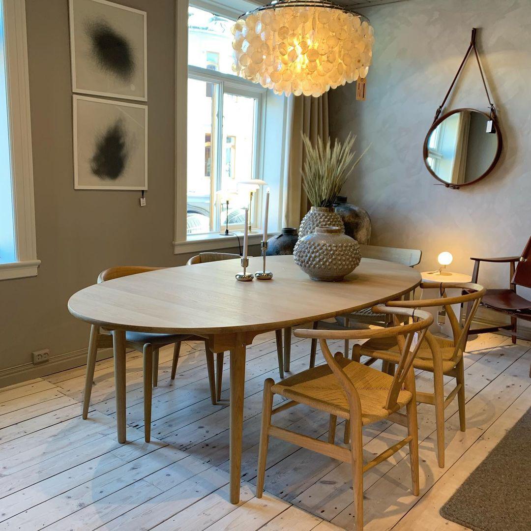 Clérachic shell chandelier glowing at the top of the frame over an oval wooden table, with a round mirror on the grey wall.