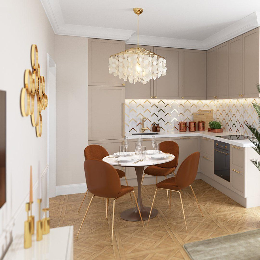 Gold-ringed Clérachic shell chandelier over a small round table in a kitchen with taupe cabinets and rust-coloured chairs.