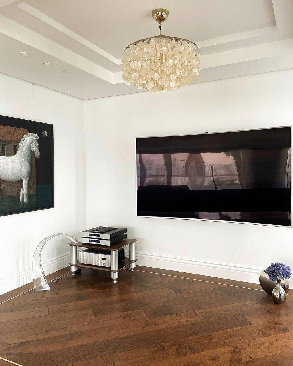 Clérachic shell chandelier on a recessed white ceiling in a living room with a dark herringbone floor and a wall-mounted screen.