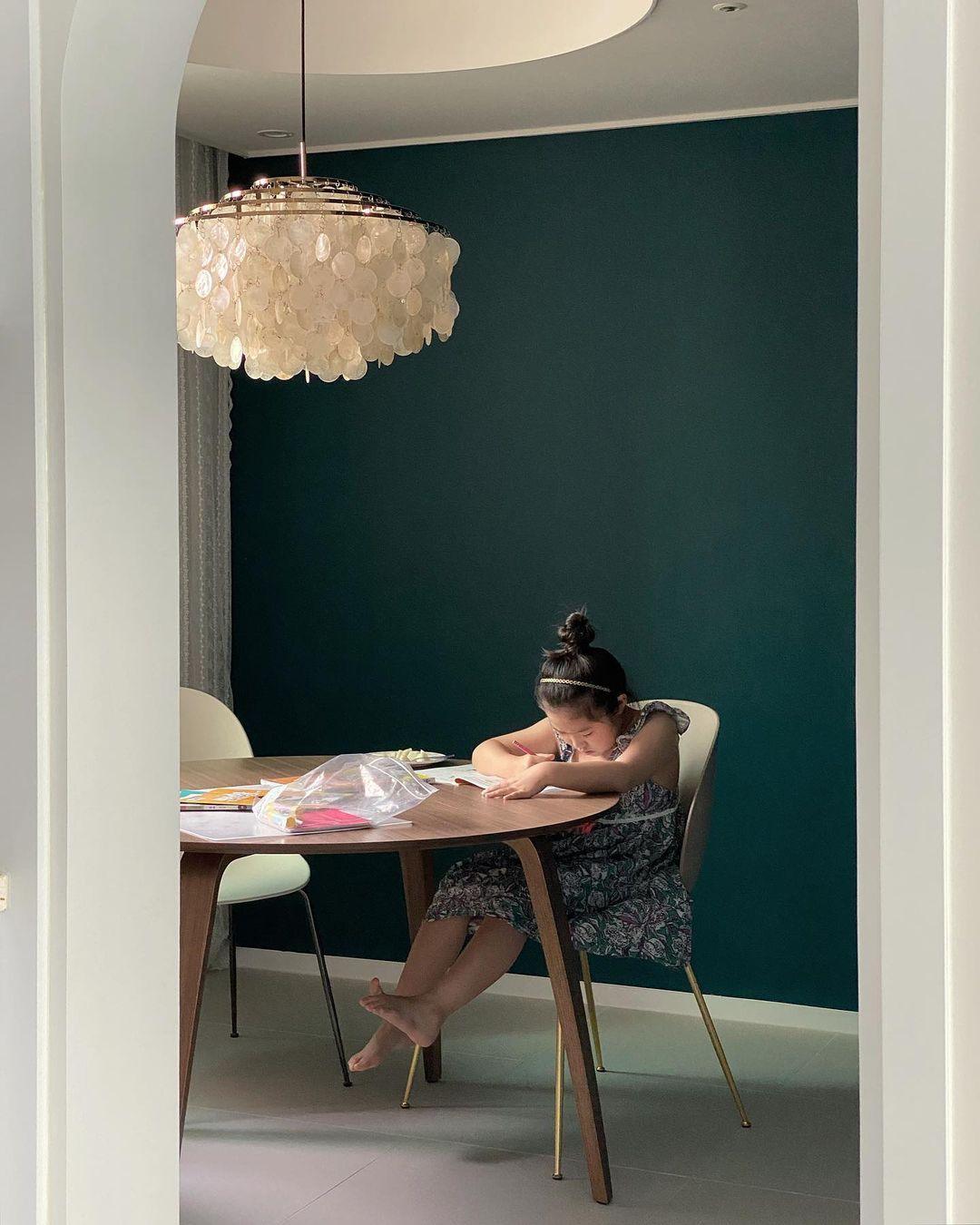 Clérachic shell chandelier above a round wooden table against a deep green wall, with a person sitting at the table.