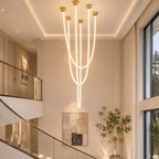 In a double-height hall beside a glass stair rail, this Clérachic pendant light drops five glowing tubes of different lengths from gold ceiling plates.