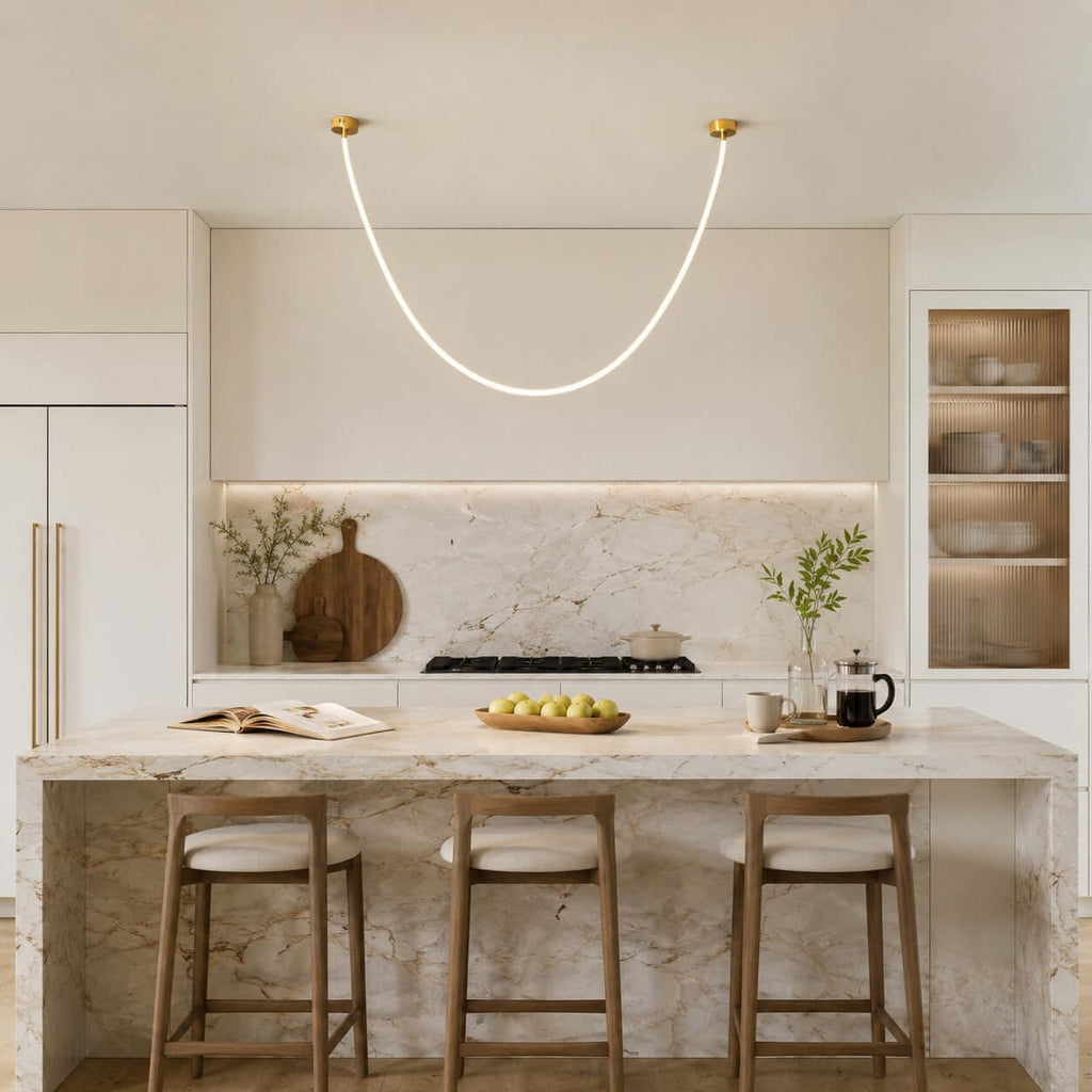 One glowing U of this Clérachic pendant light hangs over a marble kitchen island with three wooden stools.