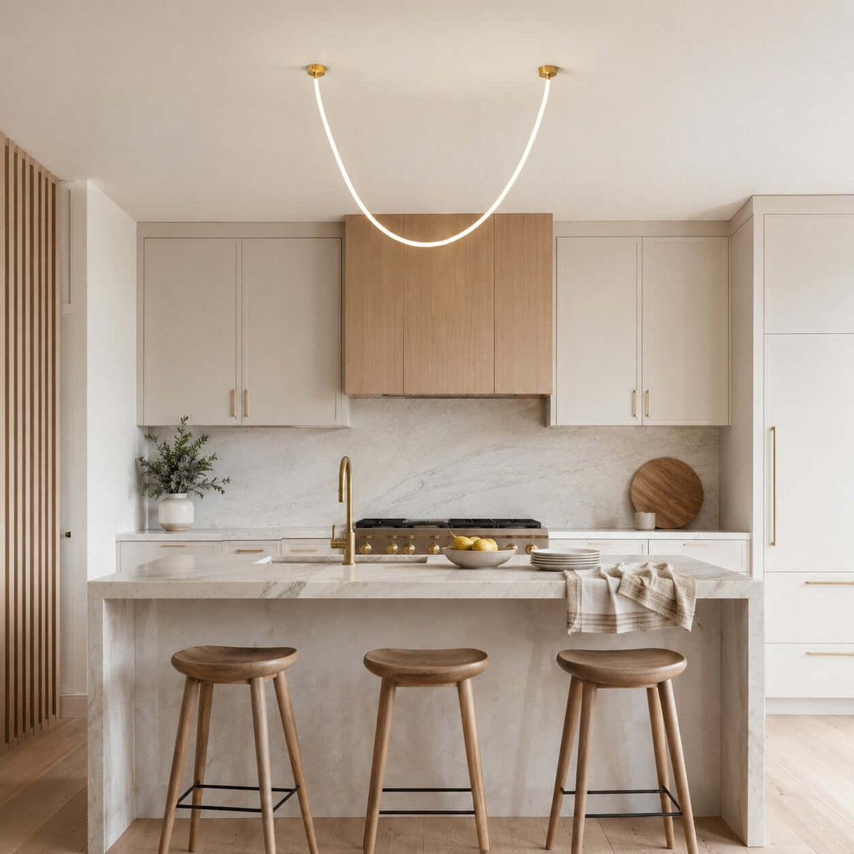 A single glowing curve of this Clérachic pendant light sits over a kitchen island with wooden stools and oak cabinets.