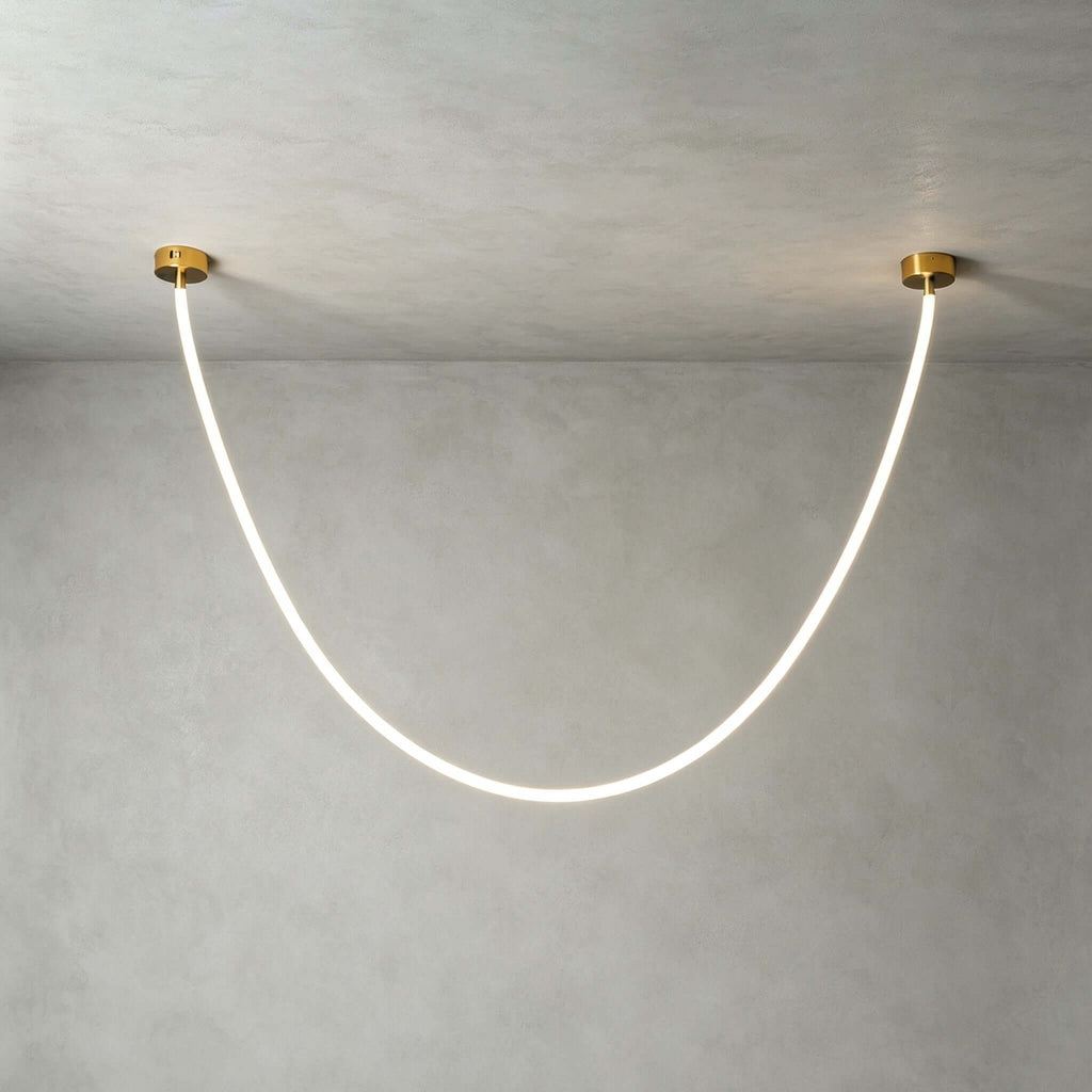 Close view of this Clérachic pendant light on a plaster-grey ceiling, the silicone tube glowing white between two gold plates.