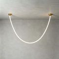 Close view of this Clérachic pendant light on a plaster-grey ceiling, the silicone tube glowing white between two gold plates.