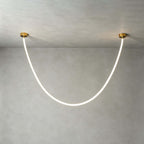 Close view of this Clérachic pendant light on a plaster-grey ceiling, the silicone tube glowing white between two gold plates.