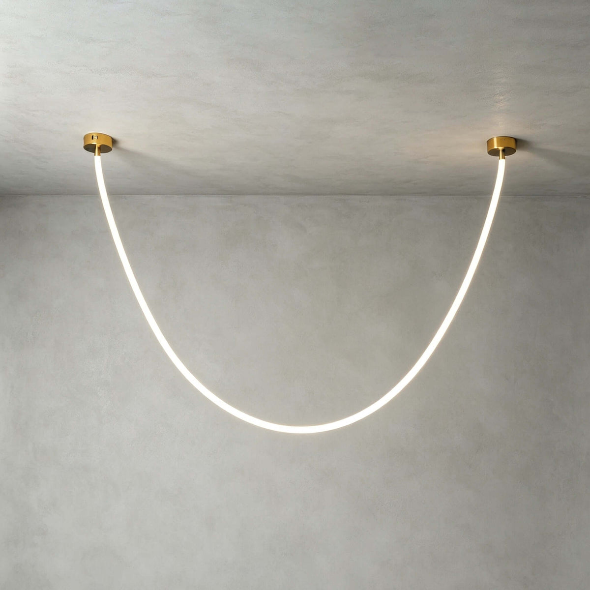 Close view of this Clérachic pendant light on a plaster-grey ceiling, the silicone tube glowing white between two gold plates.