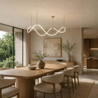 This Clérachic pendant with a glowing wave strip hangs over a rounded oak table, beside a glass wall with trees outside.