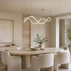 Over a long travertine-look dining table with boucle chairs, a Clérachic wave pendant glows on slim gold rods.