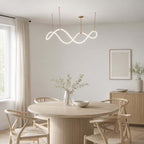 This Clérachic pendant glows above a round pedestal dining table with wishbone-style chairs, next to a bright window.