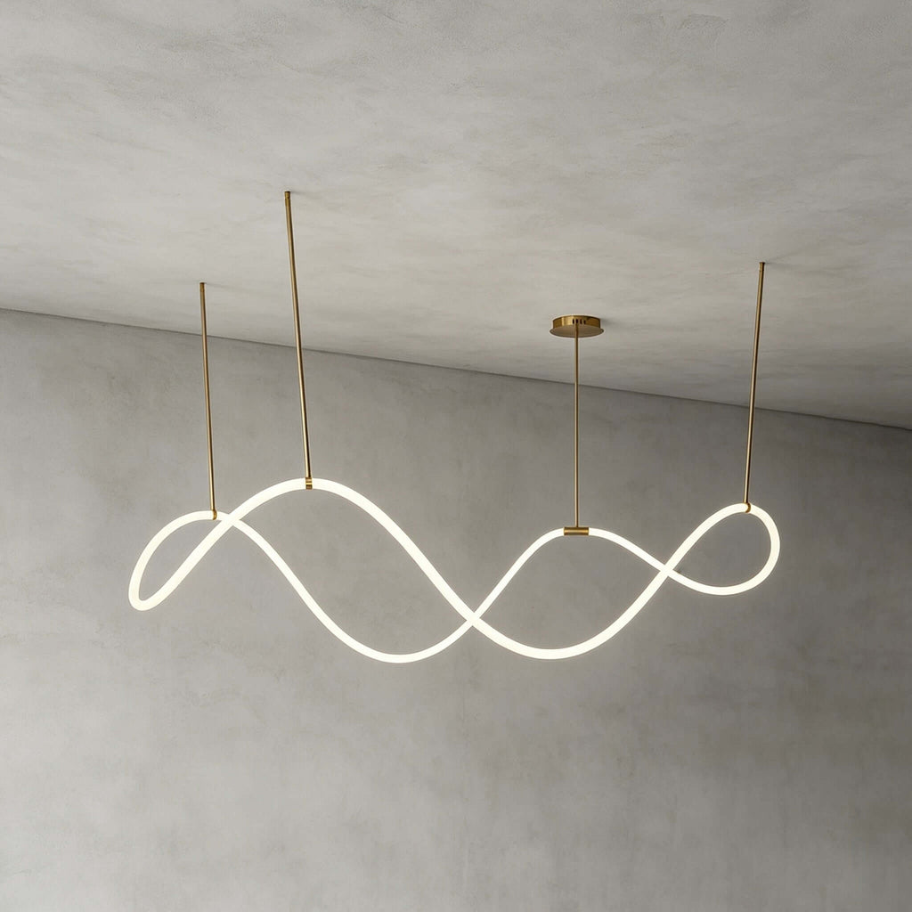 The Clérachic wave pendant lit and hung from three gold rods against a grey limewash wall, showing its continuous looping strip.
