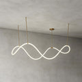 The Clérachic wave pendant lit and hung from three gold rods against a grey limewash wall, showing its continuous looping strip.