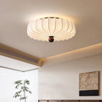A lit Clérachic flush-mount ceiling light in a bedroom with a cove-lit ceiling, a tall plant and a textured wall panel.