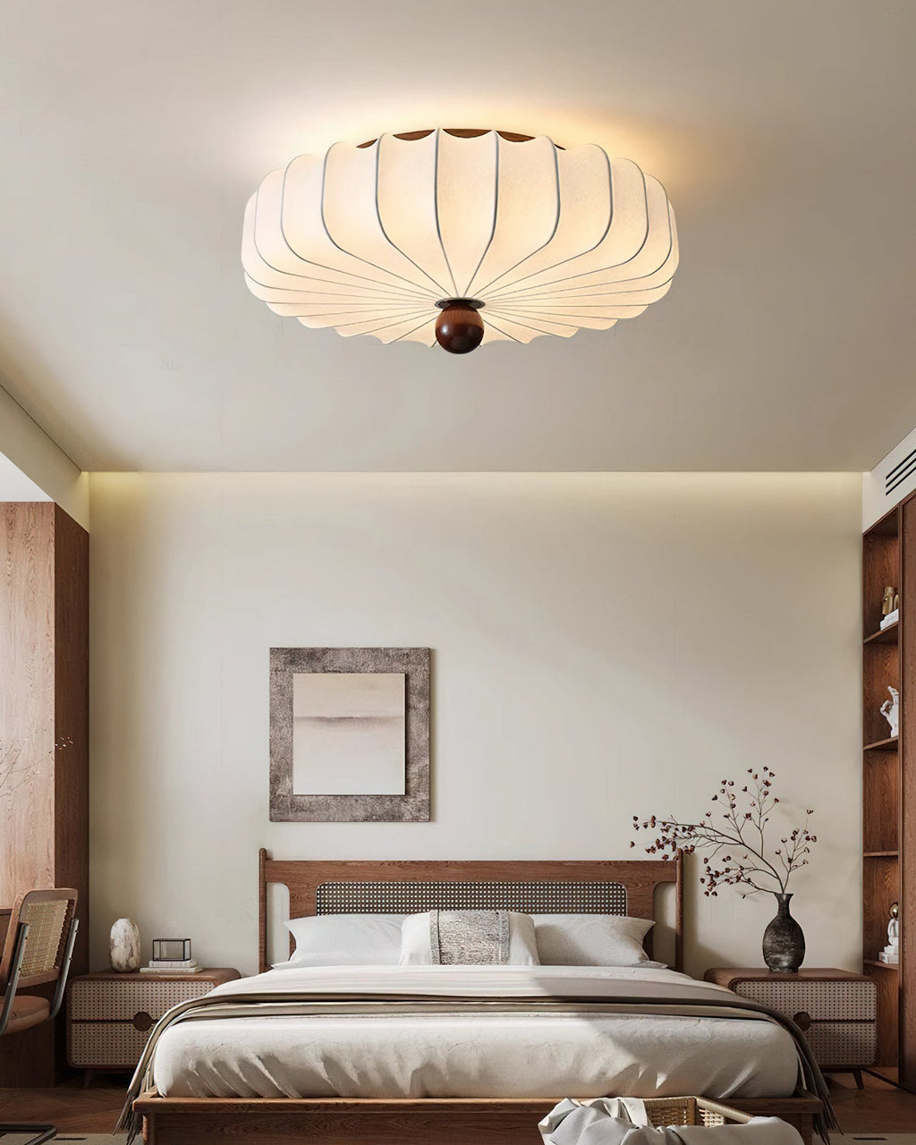A Clérachic ceiling light lit above a calm bedroom, with a framed print, a wooden bed and shelves in the background.