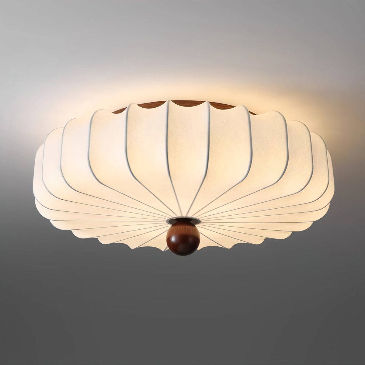 Close view from below of the pleated shade and walnut-colour finial of this Clérachic ceiling light, lit against a grey ceiling.