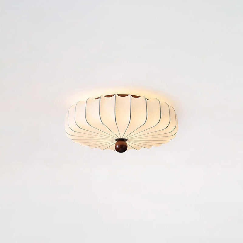 Lit Clérachic flush-mount ceiling light with a soft glow around its pleated shade, on a pale ceiling.