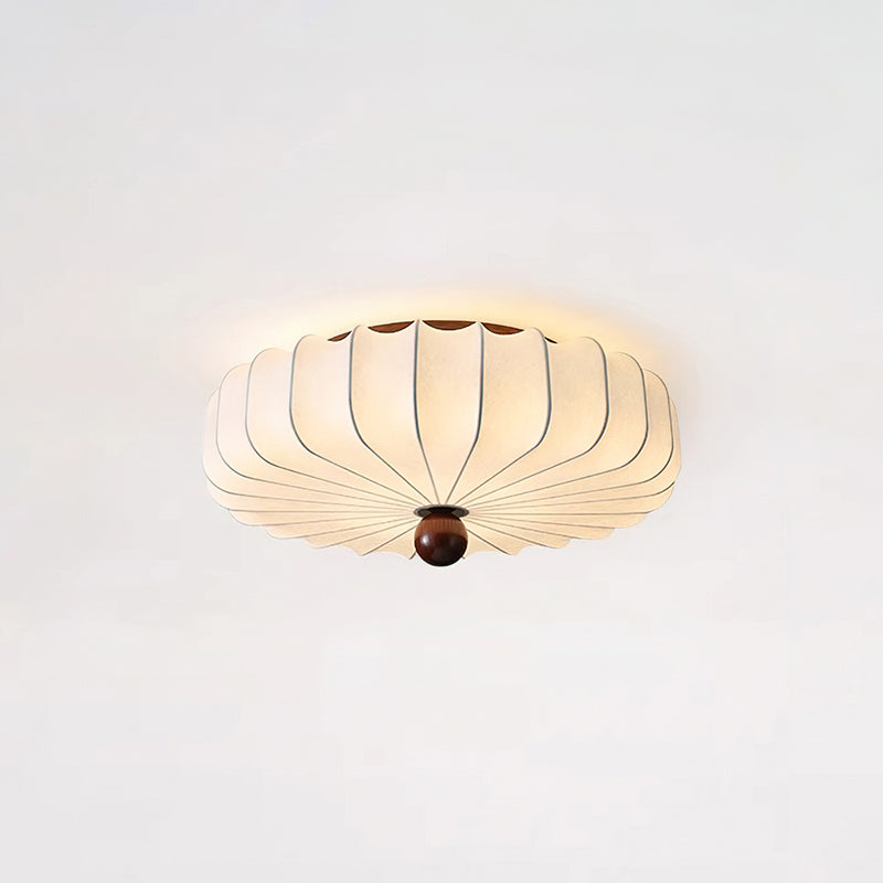 This Clérachic ceiling light sits close to a pale ceiling, its pleated shade glowing and a walnut-colour finial at the centre.