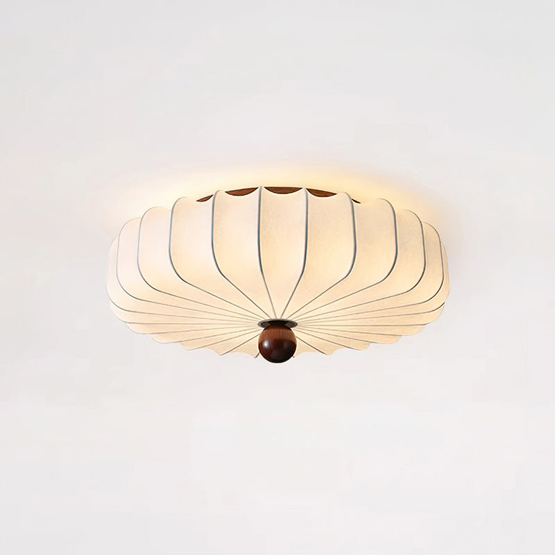 Angled view of the scalloped pleated shade and walnut-colour finial of this Clérachic ceiling light, lit on a light ceiling.